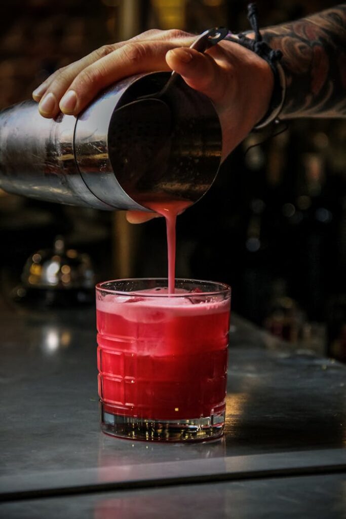 A bartender pours a vibrant red cocktail into a glass on a bar counter.